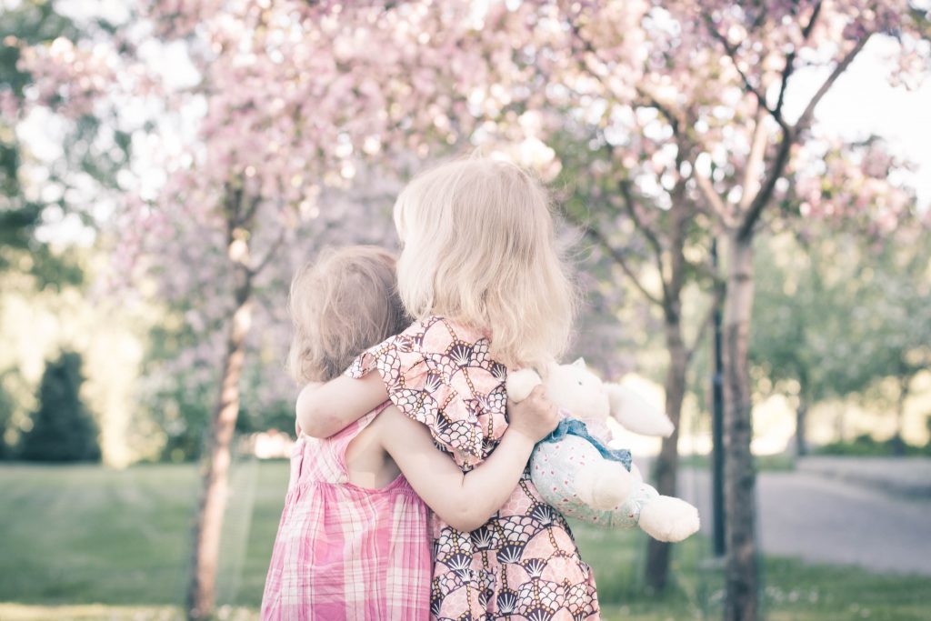 kaksi lasta halaavat toisinaan hempeässä kesäkuvassa