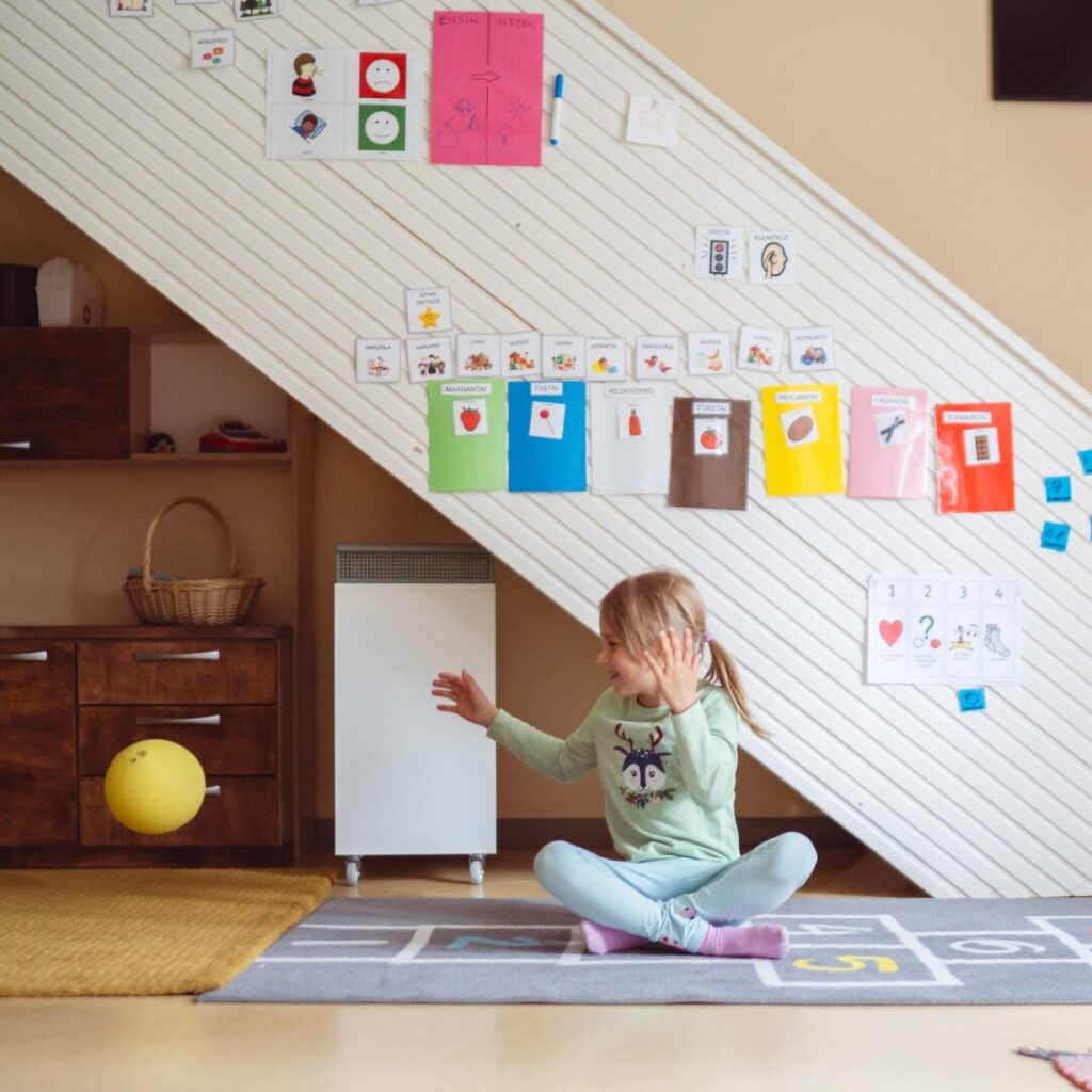 Vihreäpaitainen lapsi leikki pallolla päiväkodin sisätiloissa.